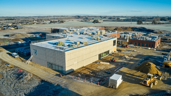 Dronefoto af byggepladsen med hallen i forgrunden og frostklædte marker i baggrunden.